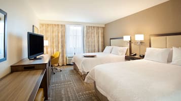 Une chambre d’hôtel avec deux lits, un bureau avec une télévision, une chaise et une fenêtre avec des rideaux.