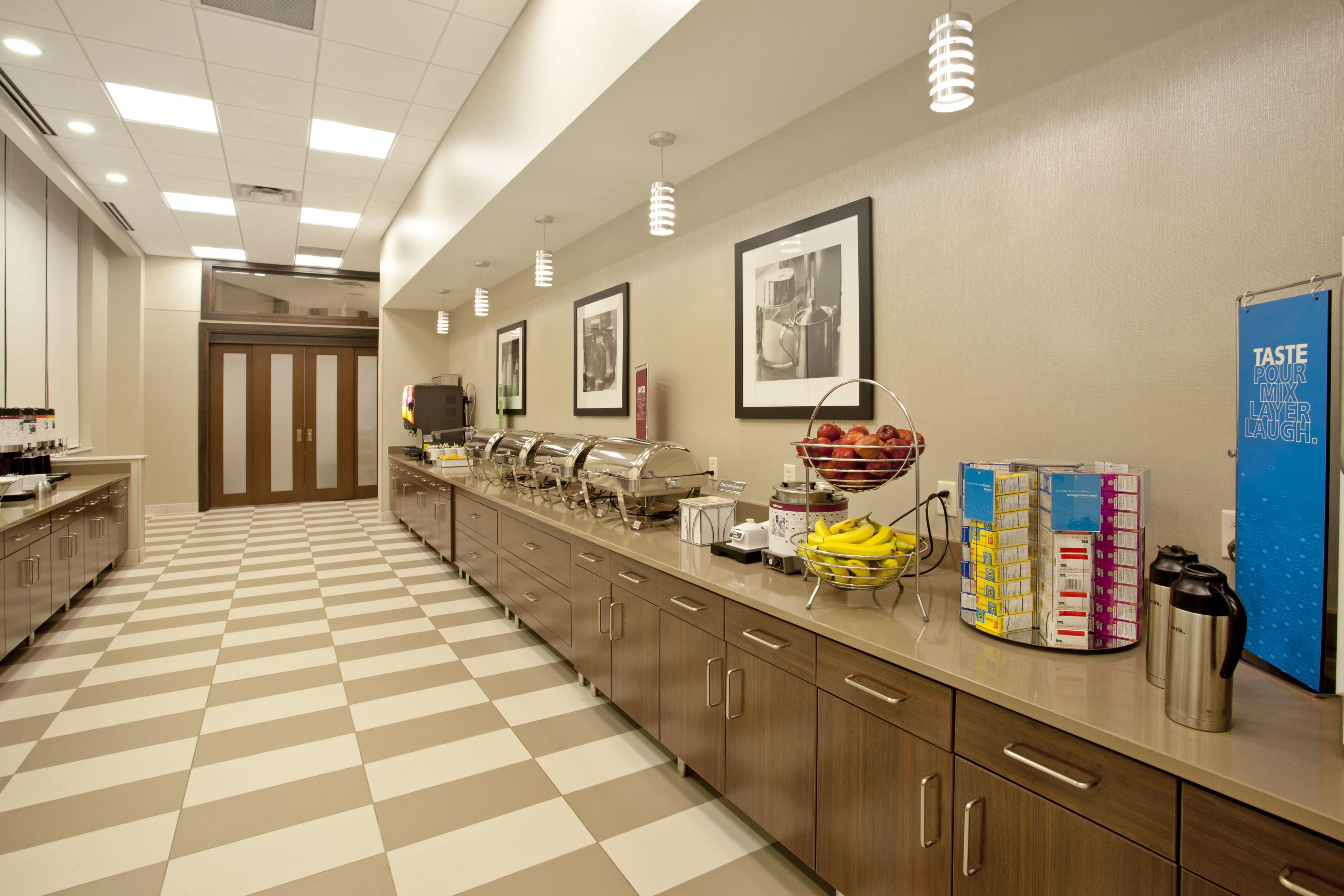 A hotel kitchen with a checkered floor, stainless steel appliances, and a buffet area with food items and condiments.