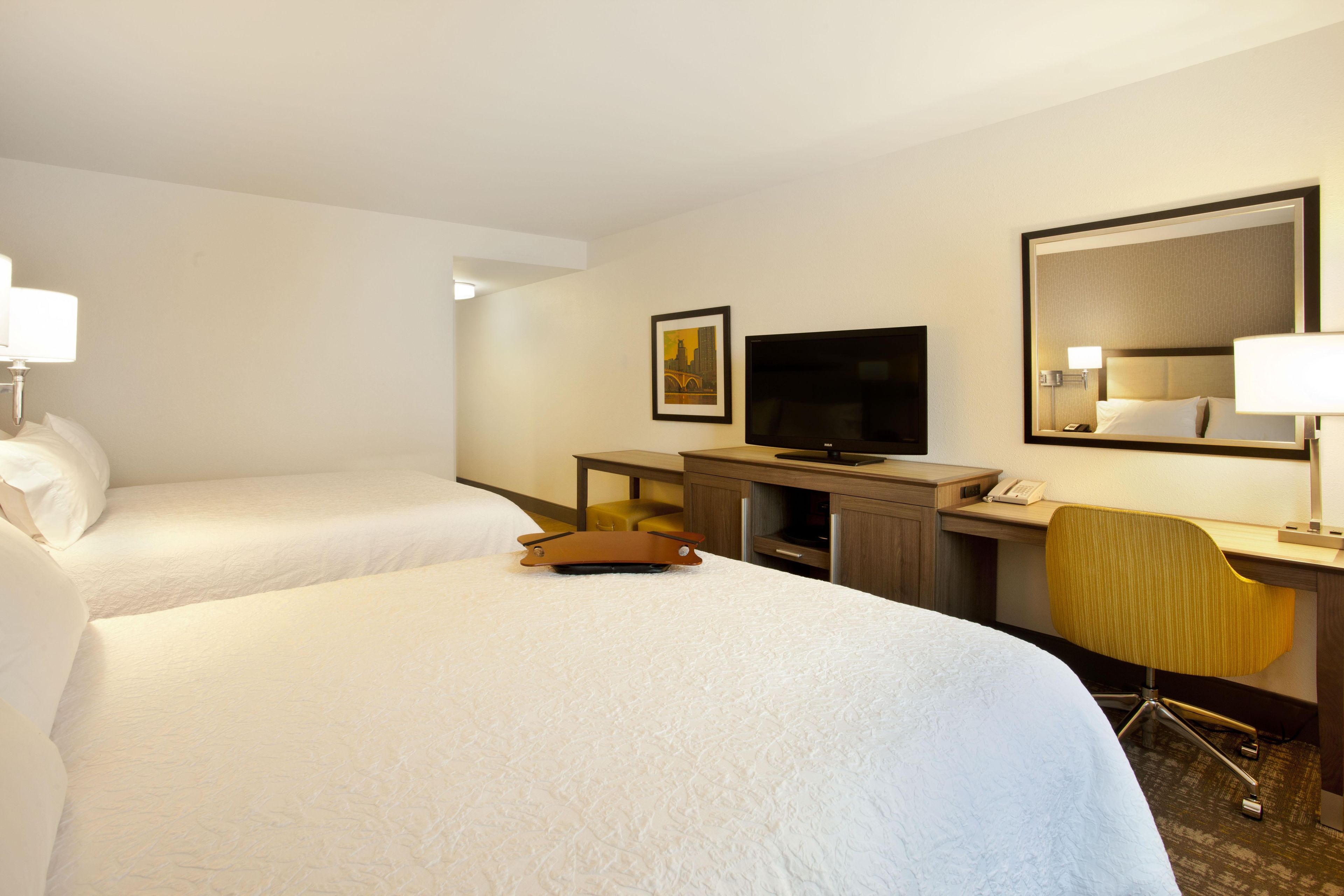 A hotel room with two beds, a desk with a chair, a television, and a mirror.