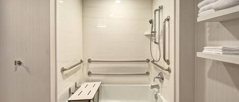 Un baño moderno con ducha a ras de suelo, barras de apoyo, un perchero y una estantería con toallas dobladas.