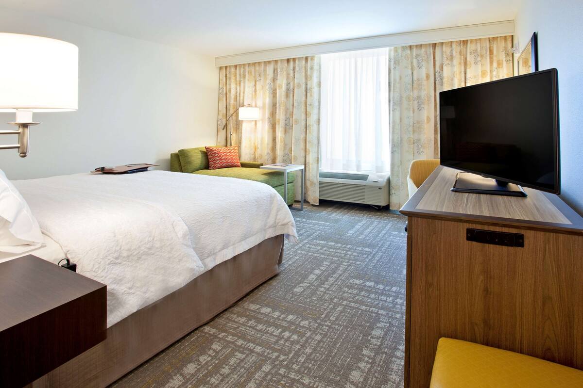A hotel room with a bed, a desk, a television, and a window with curtains.