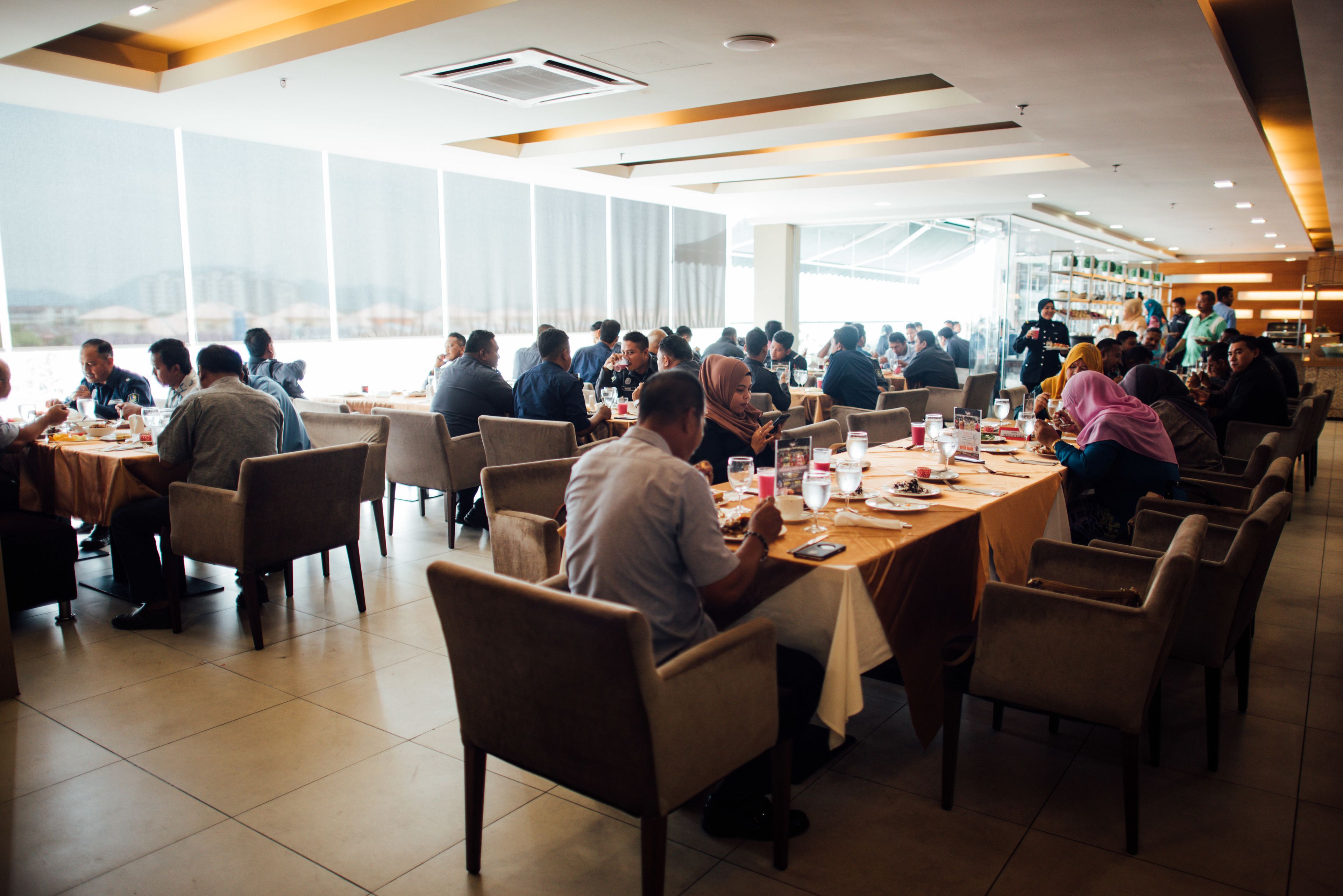 Un restaurant spacieux, doté de nombreuses tables et chaises, de grandes fenêtres offrant une vue sur le paysage urbain et d’un aménagement intérieur moderne.