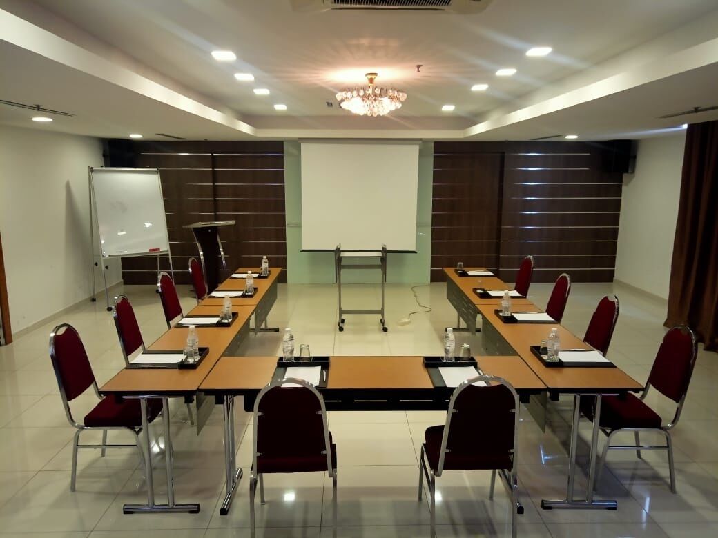 A conference room with long tables, red chairs, a whiteboard, and a projector screen.