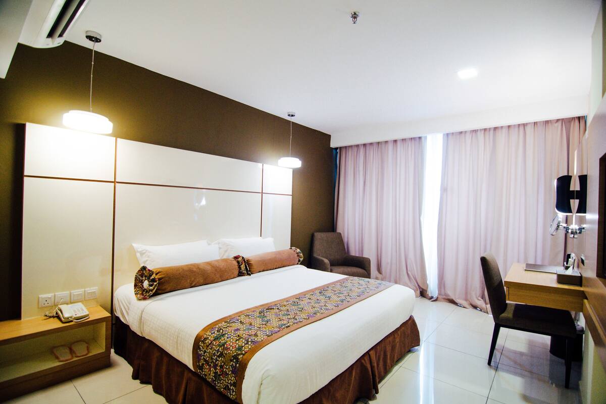 A hotel room with a large bed, a desk, a chair, and a TV.