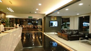 Un moderno vestíbulo de hotel con recepción, zona de estar y una pantalla de televisión.
