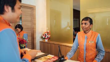 A hotel reception area with a wooden reception desk, a name tag on the staff member, and a flower arrangement on the counter.