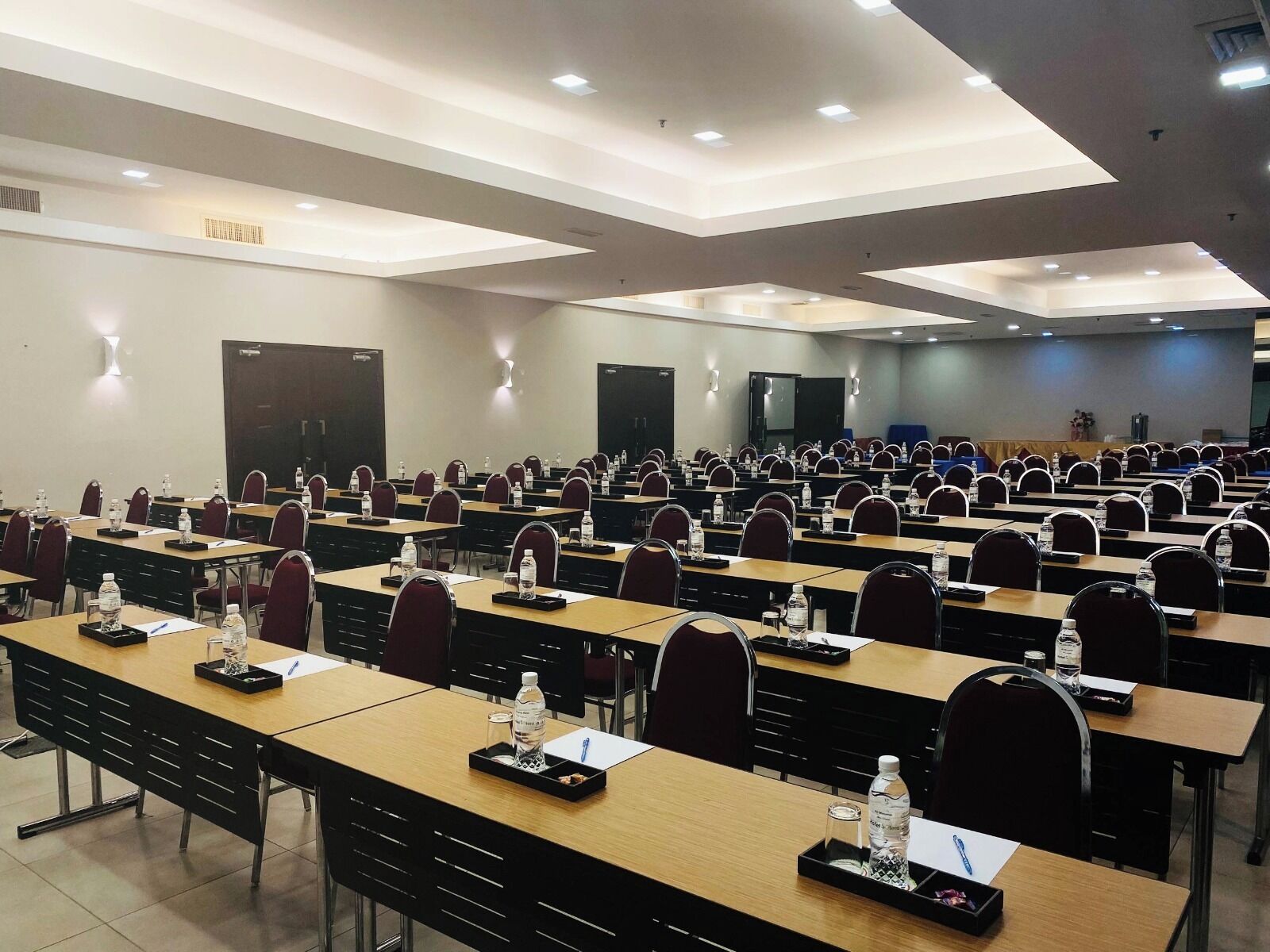 Un salón de conferencias con filas de mesas y sillas, equipado con botellas de agua y tarjetas de identificación.