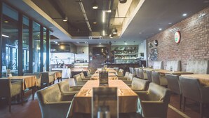 Un restaurante con pared de ladrillo, ventanas amplias y varias mesas y sillas.