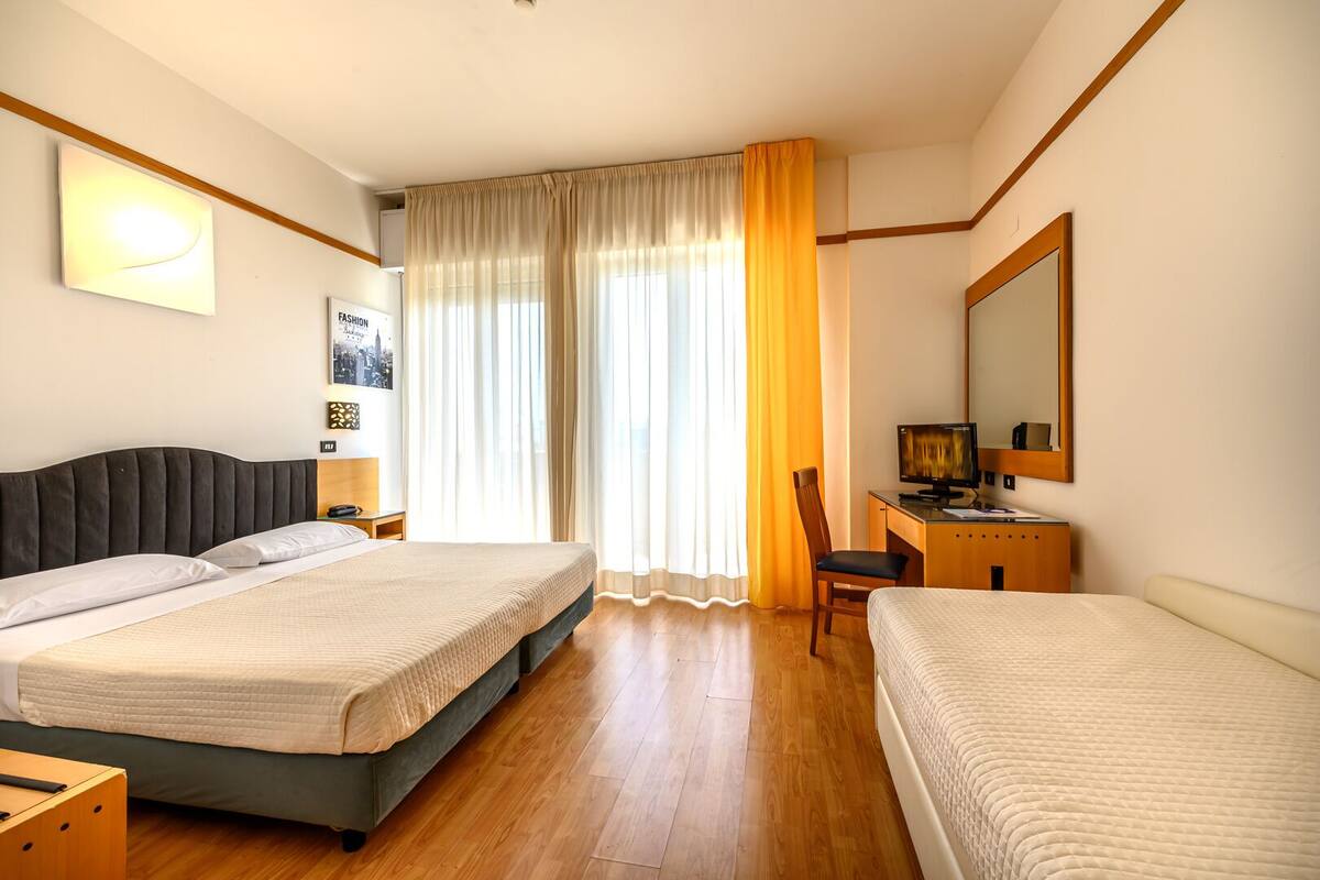 A hotel room with a bed, a desk, a chair, a mirror, and a window with curtains.
