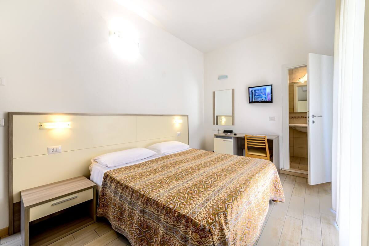 A hotel room with a bed, bedside table, desk, chair, and a television on the wall.