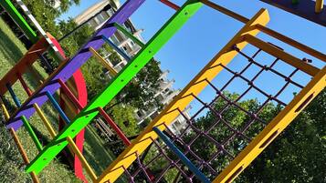 Kids can play and climb on the playground structure with bars and beams, surrounded by trees and a building.