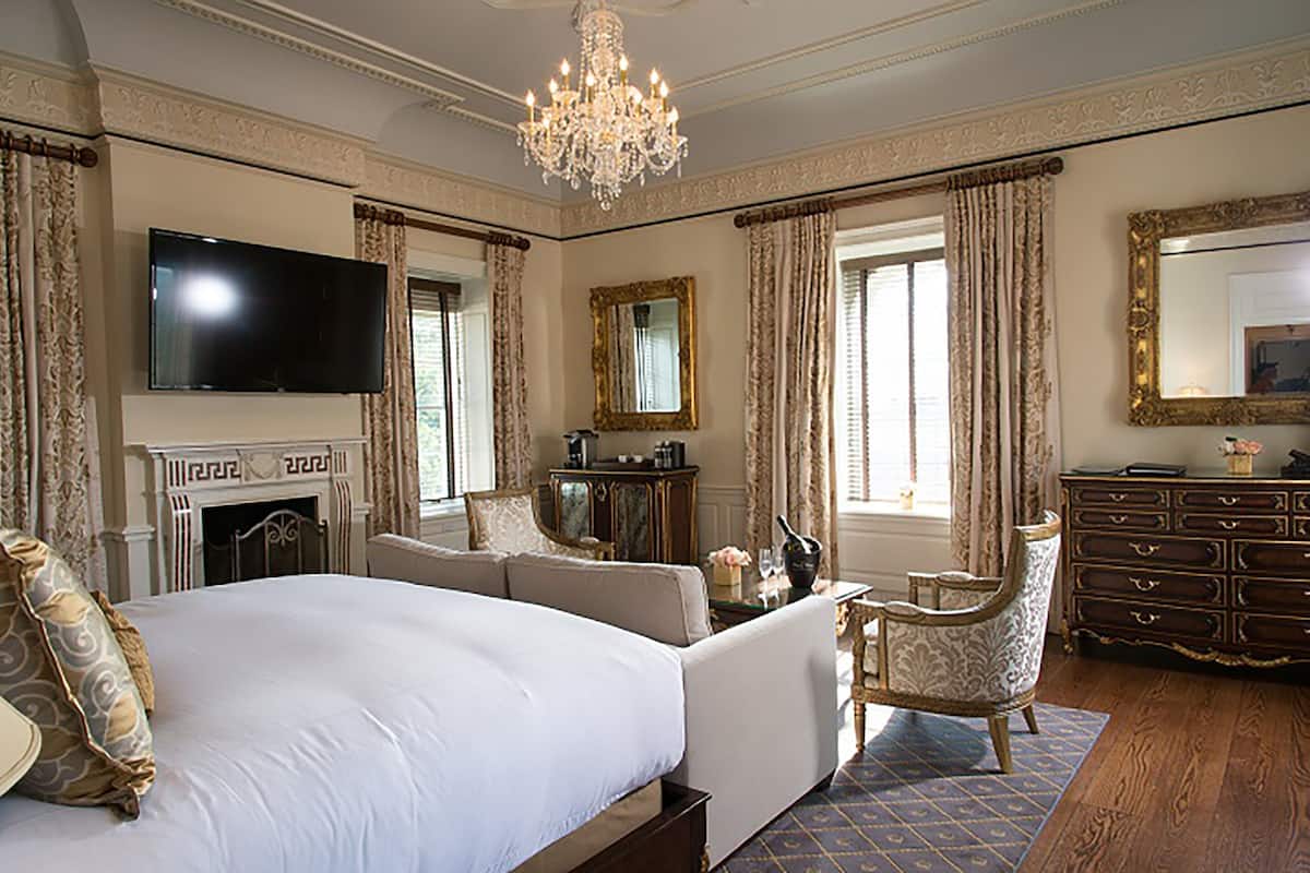 A spacious bedroom with a large bed, a television, a fireplace, and a chandelier.