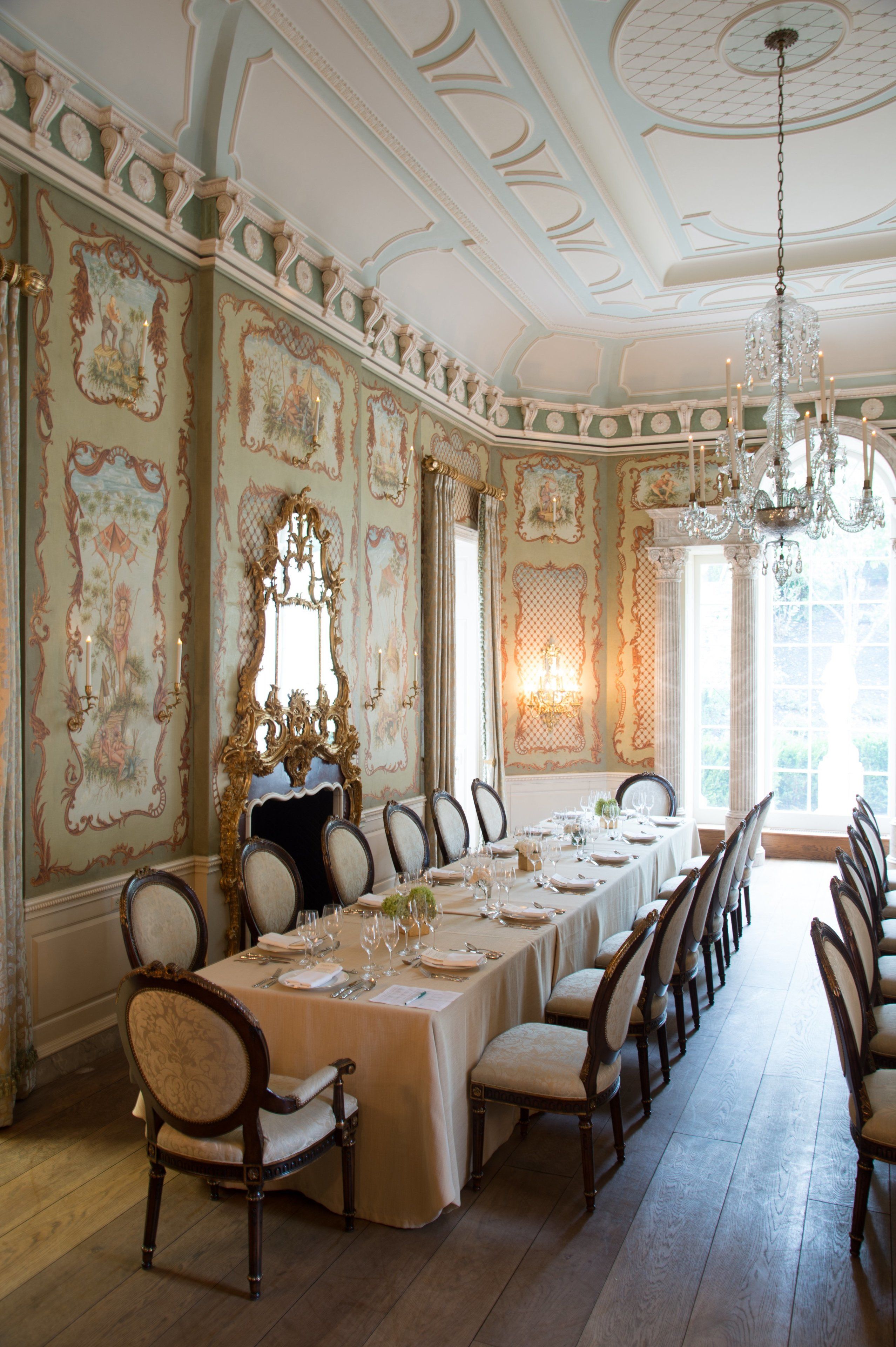 A formal dining room with a long table set for a meal, ornate wall decorations, and a chandelier.