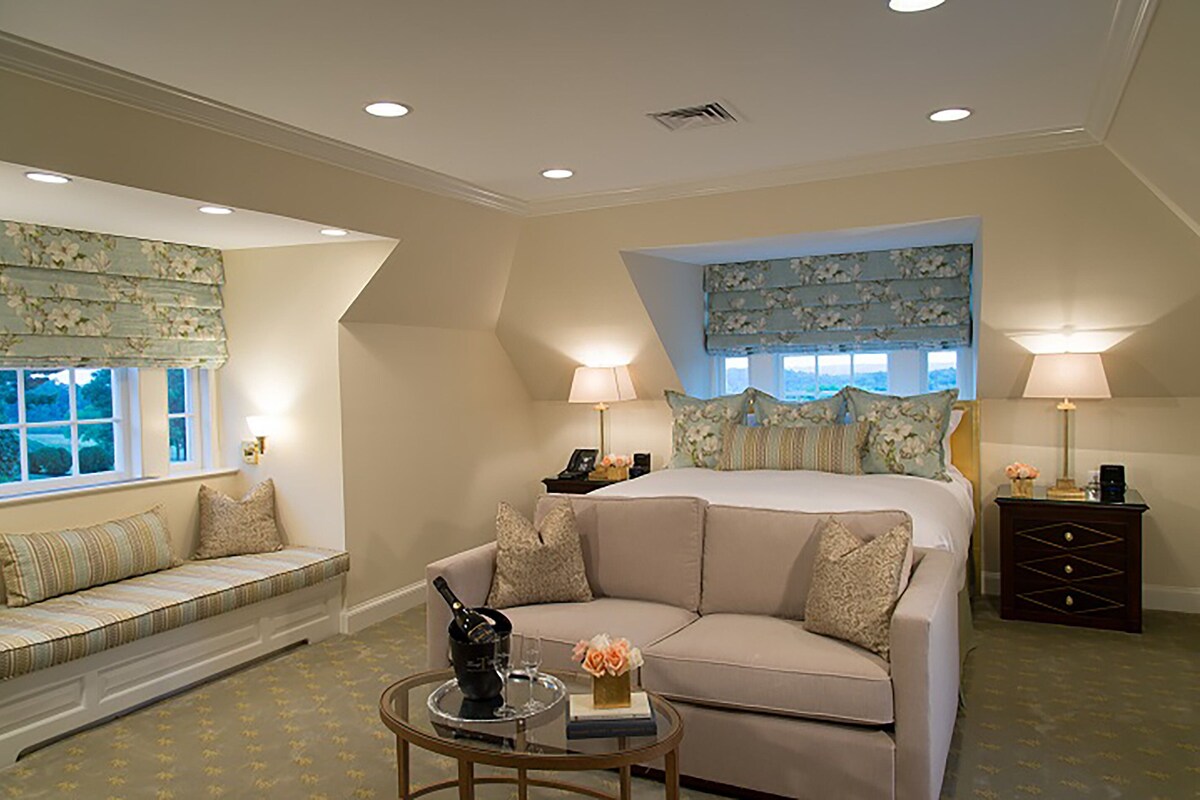 A bedroom with a large bed, a sofa, a small table with a bottle and glasses, and two lamps.
