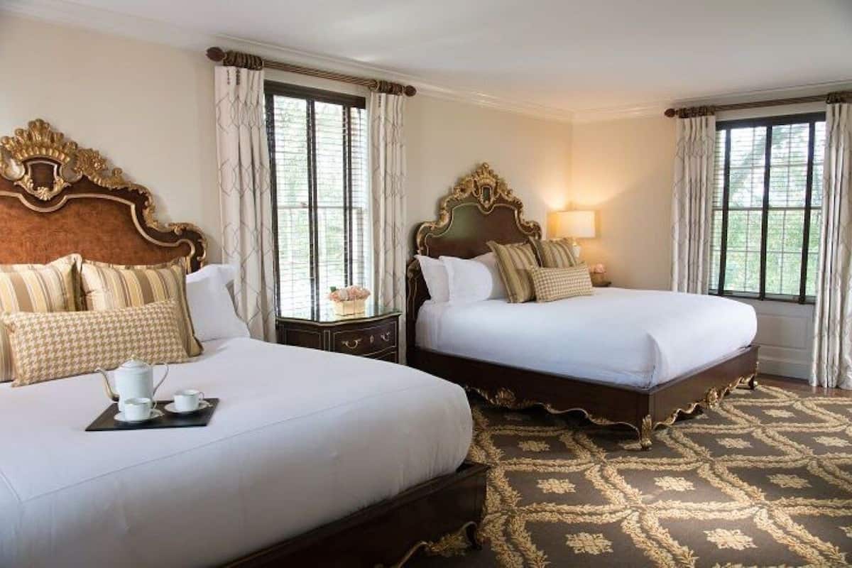 A hotel room with two beds, a large window, a decorative headboard, and a patterned carpet.