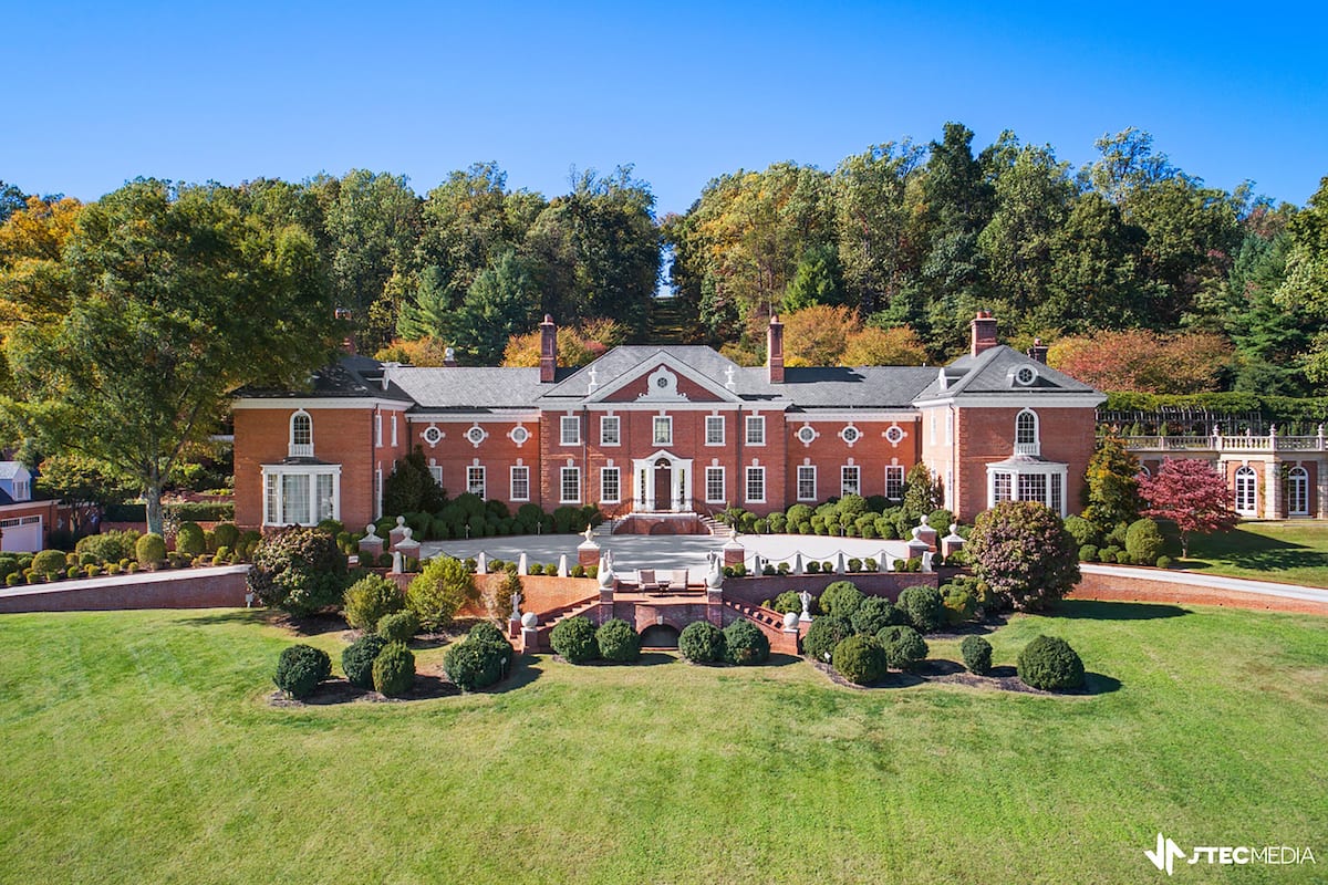 A large, red-brick building with a symmetrical facade, a central entrance, and a well-manicured lawn with trimmed bushes and a fountain.