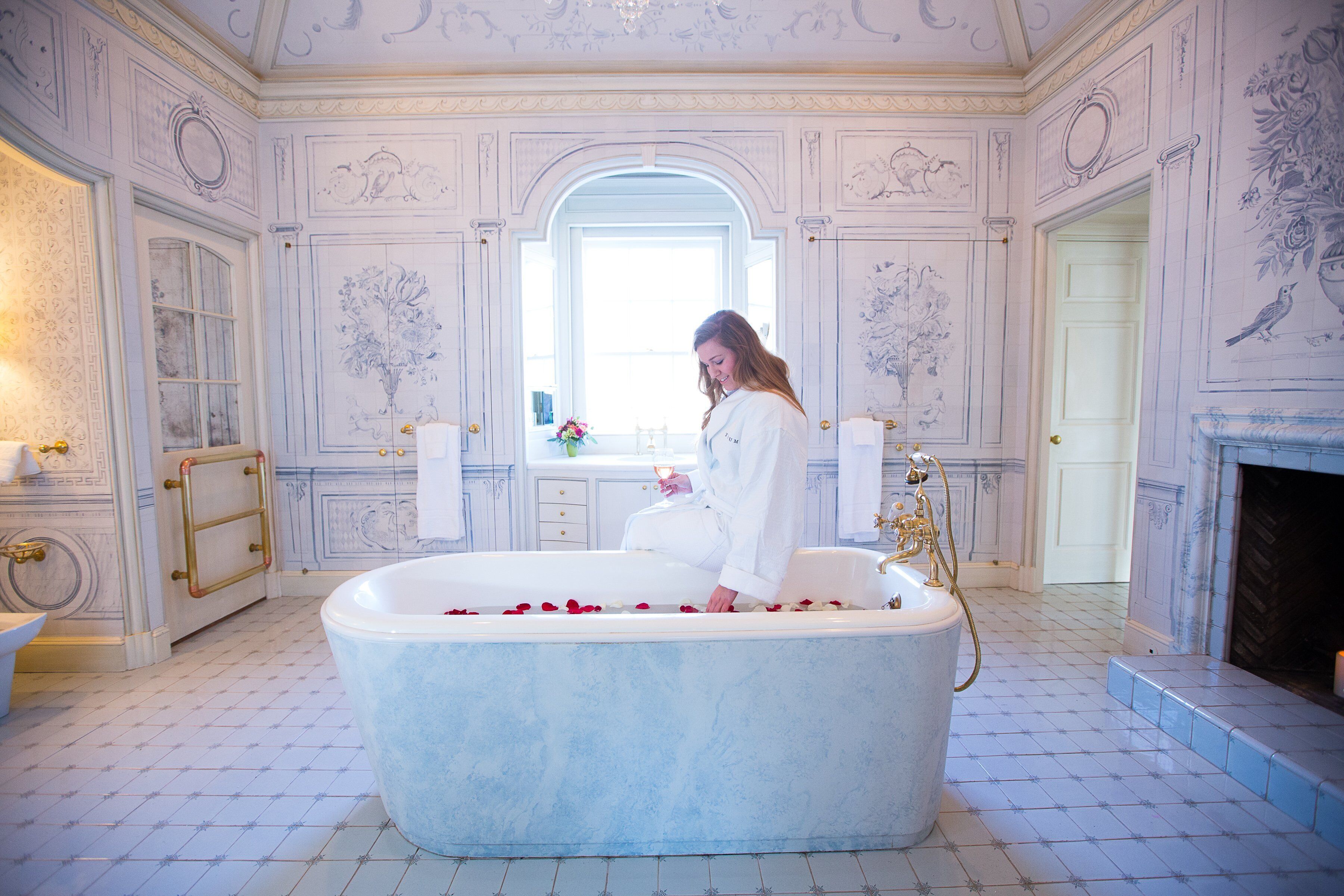 A luxurious bathroom with a large bathtub, ornate wall decorations, and a mirror.