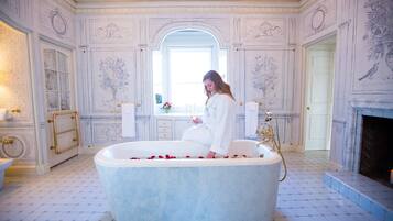 A luxurious bathroom with a large bathtub, ornate wall decorations, and a mirror.