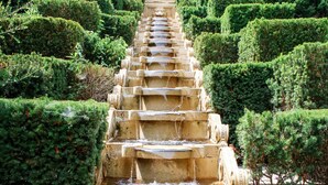 Une fontaine à étages, avec plusieurs niveaux et de l’eau qui dévale en cascade, le tout entouré de haies soigneusement taillées.