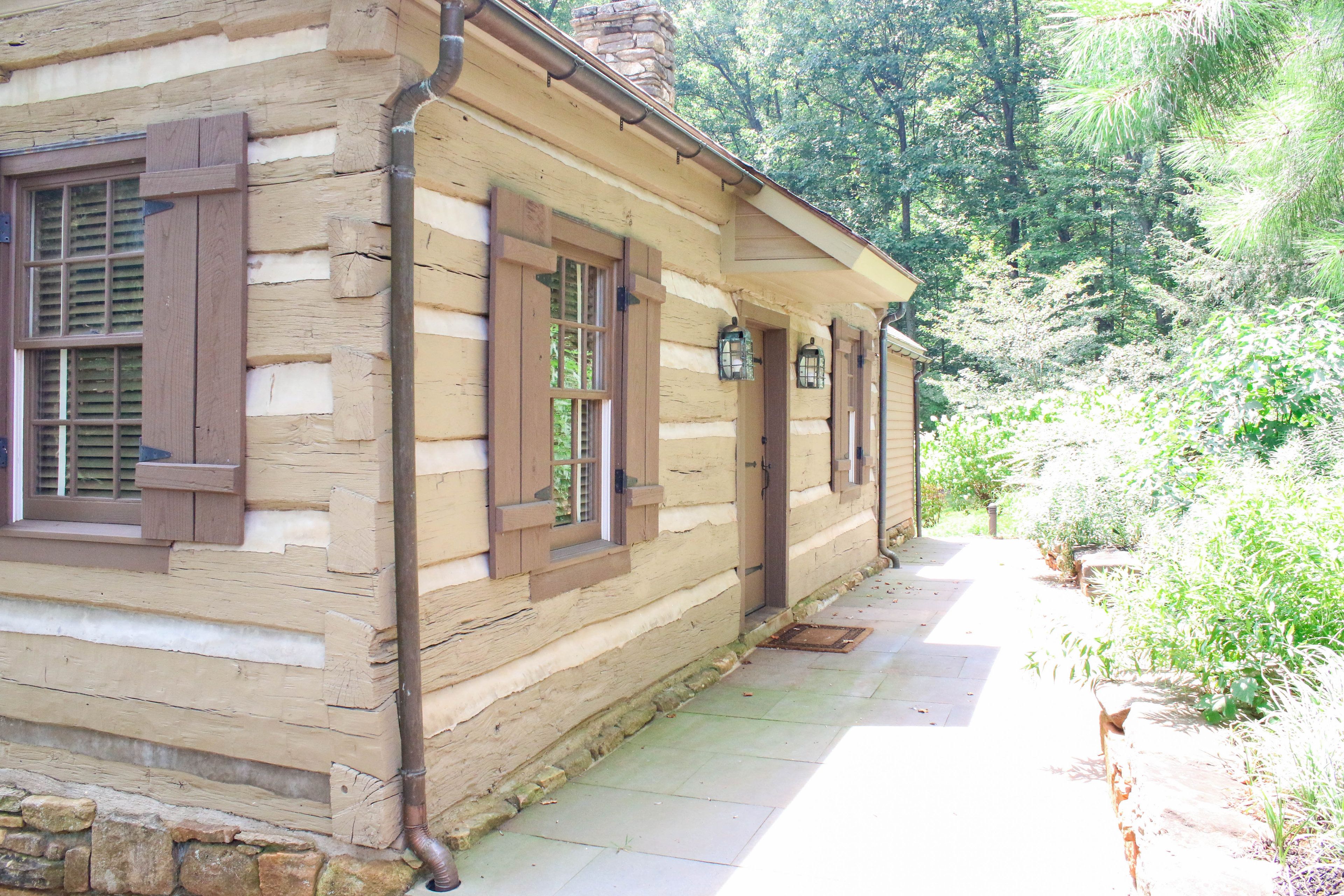 A log cabin with a stone foundation, wooden shutters, and a stone chimney.