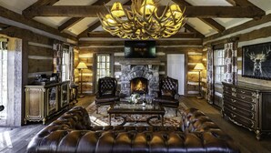 L’intérieur d’une cabane en rondins, avec une cheminée en pierre, des meubles en cuir et un lustre.