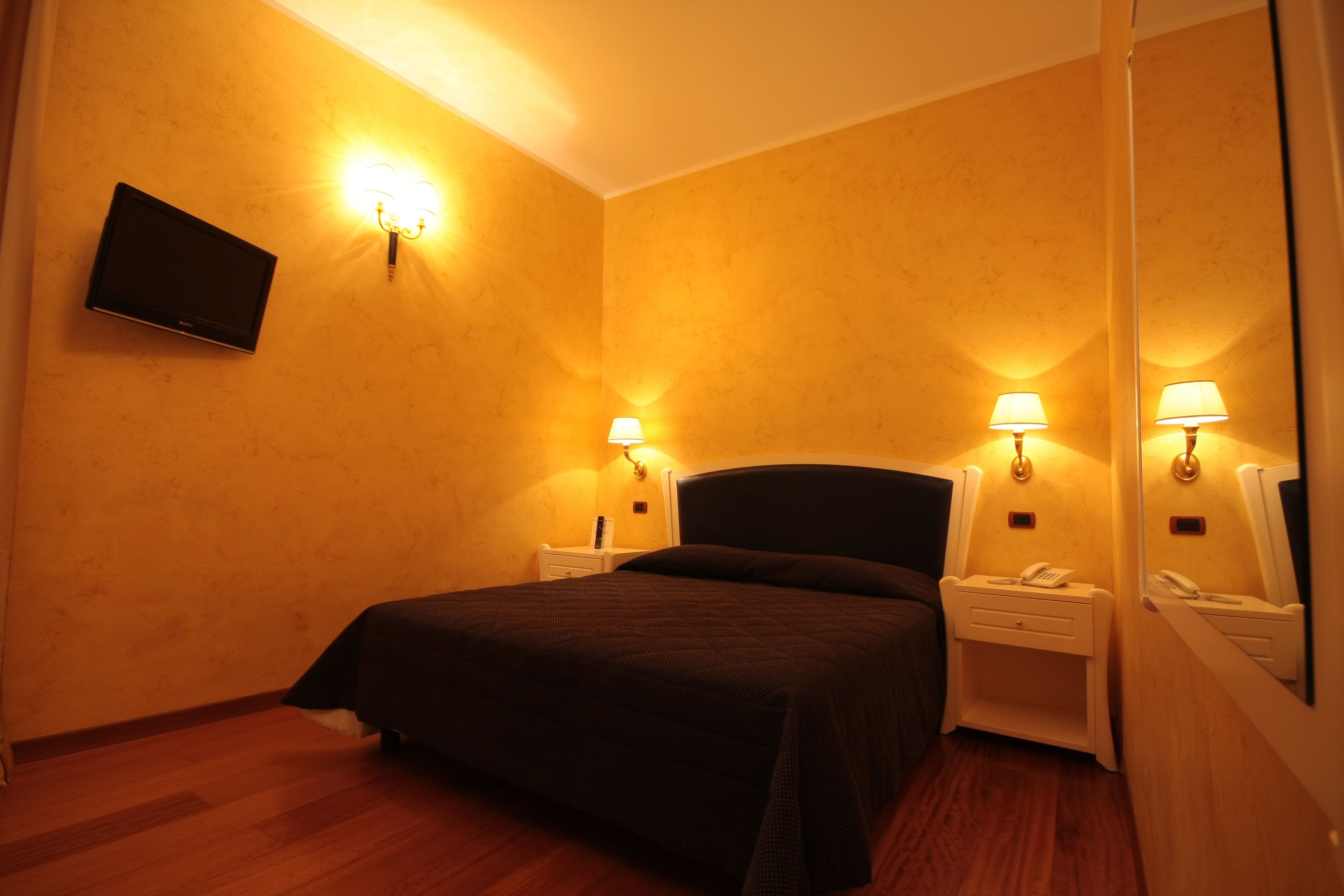 Habitación de hotel con cama, mesitas de noche, lámparas, televisor de pantalla plana y espejo.