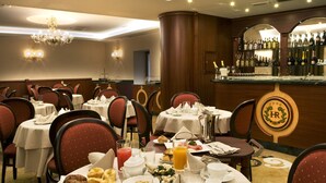 Un comedor de hotel con mesas redondas, sillas tapizadas de rojo y una barra con selección de vinos.
