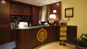Un mostrador de recepción con detalles de madera, un certificado enmarcado, una lámpara y una planta.