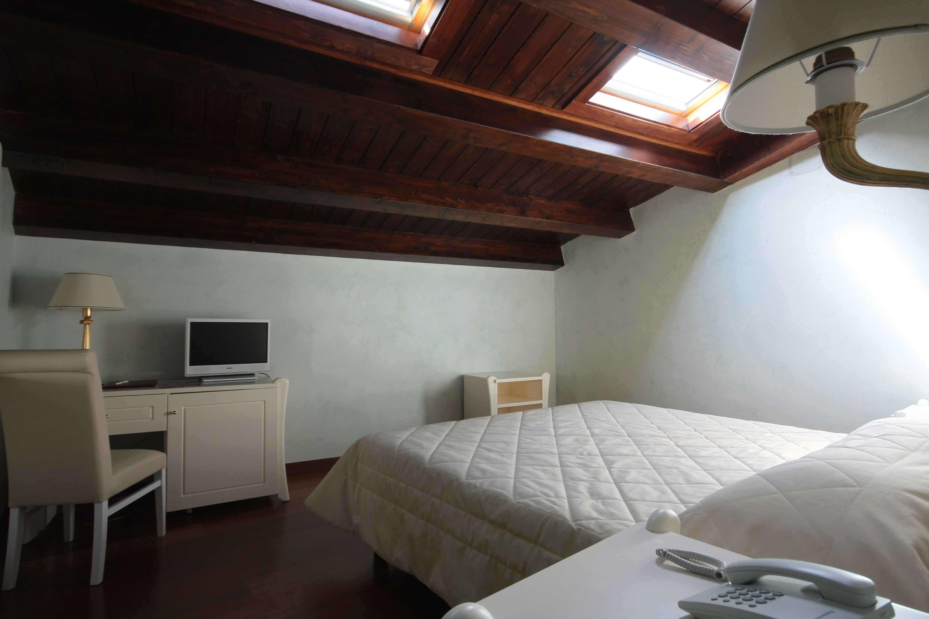 A bedroom with a bed, a desk with a computer, a lamp, and a telephone.