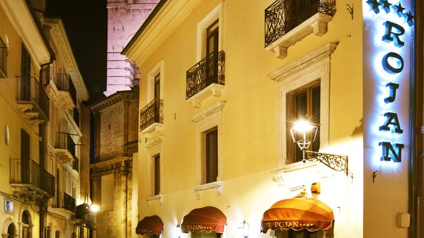 Hotel Rojo, un hotel con una torre destacada al fondo, una calle adoquinada y áreas de estar al aire libre con sombrillas.