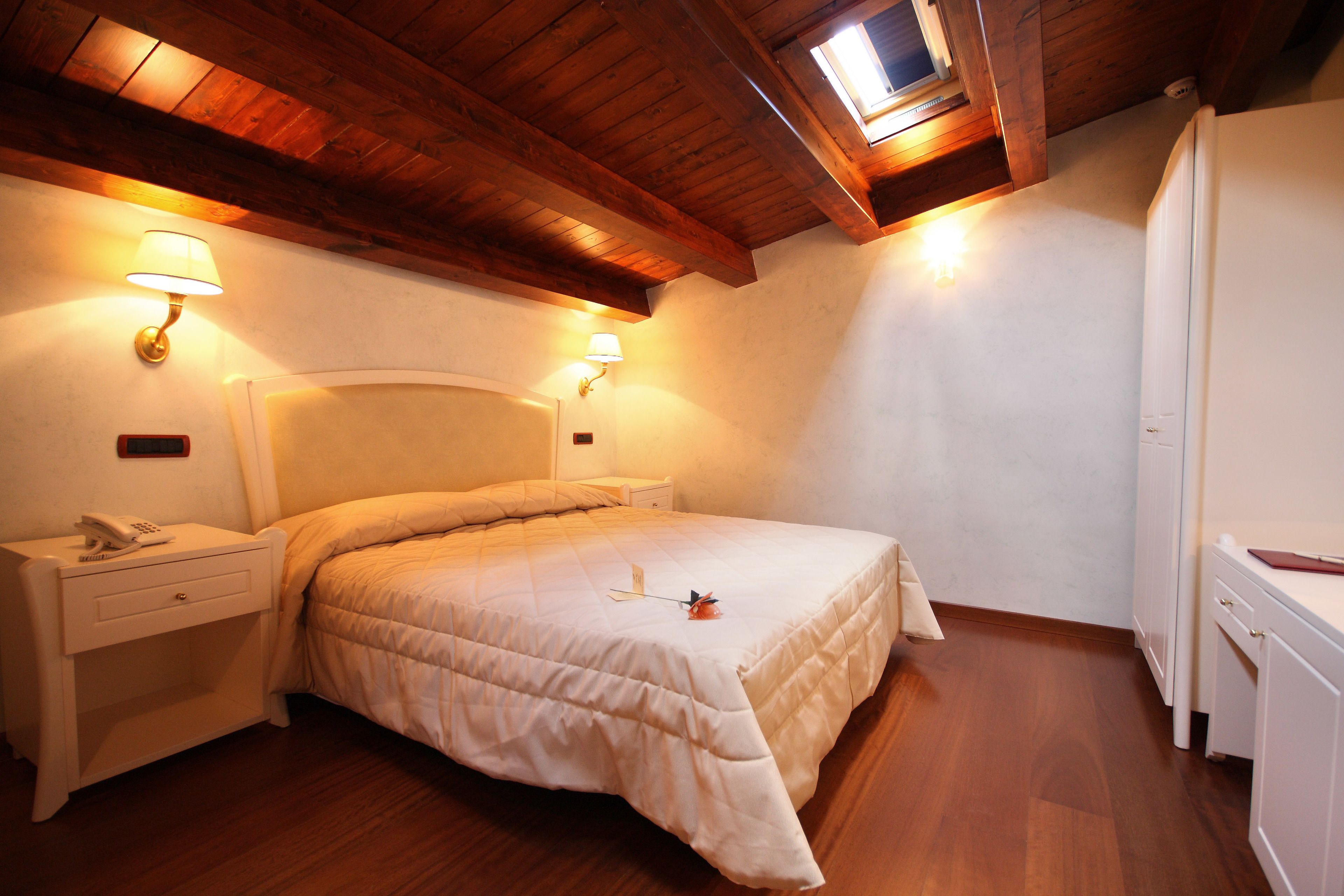 Ein Schlafzimmer mit Holzboden, einem Bett mit beige farbenem Duvet, Nachttischlampen, einem Nachttisch mit Telefon und einem Heizkörper.