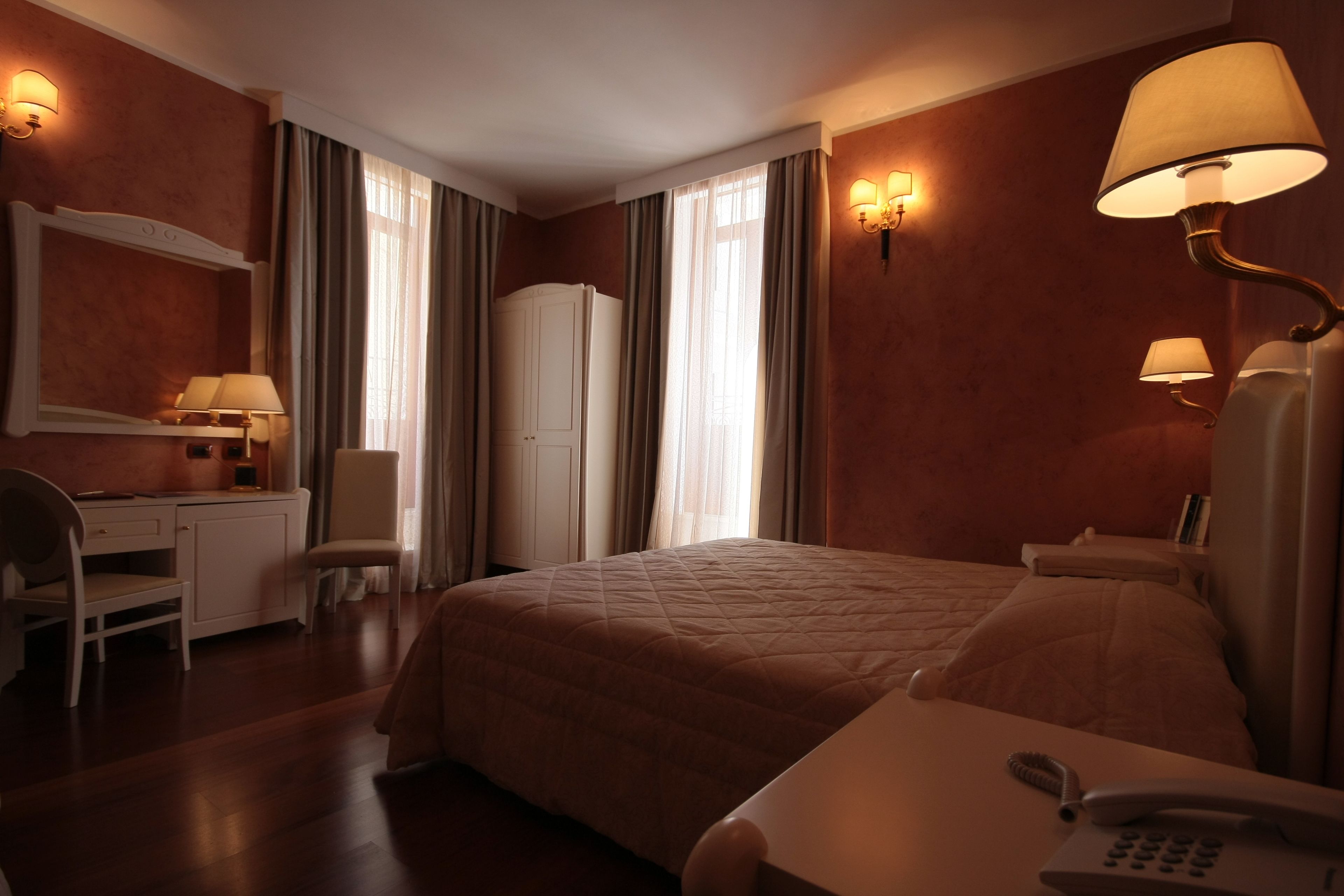 A hotel room with a bed, desk, chair, and two bedside lamps.
