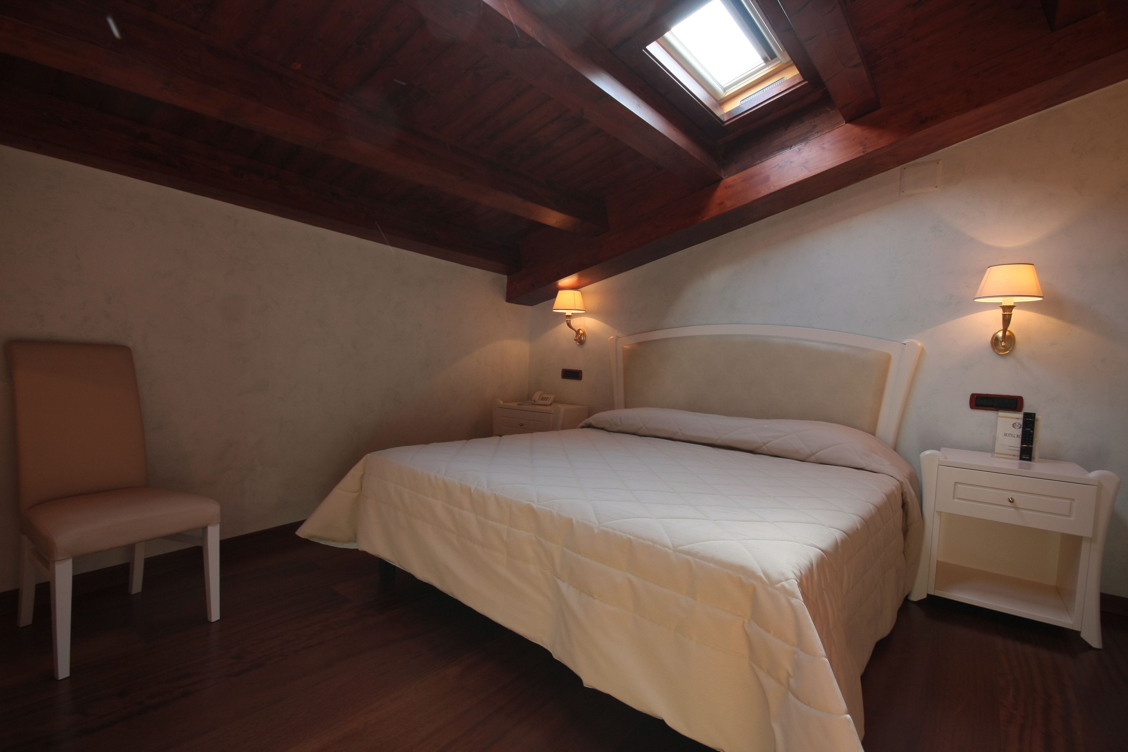 A bedroom with a bed, a chair, a nightstand, and a skylight.