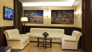 Un hall de hotel con un sofá de cuero blanco, dos sillones, una mesita de centro de mármol y un televisor en la pared.