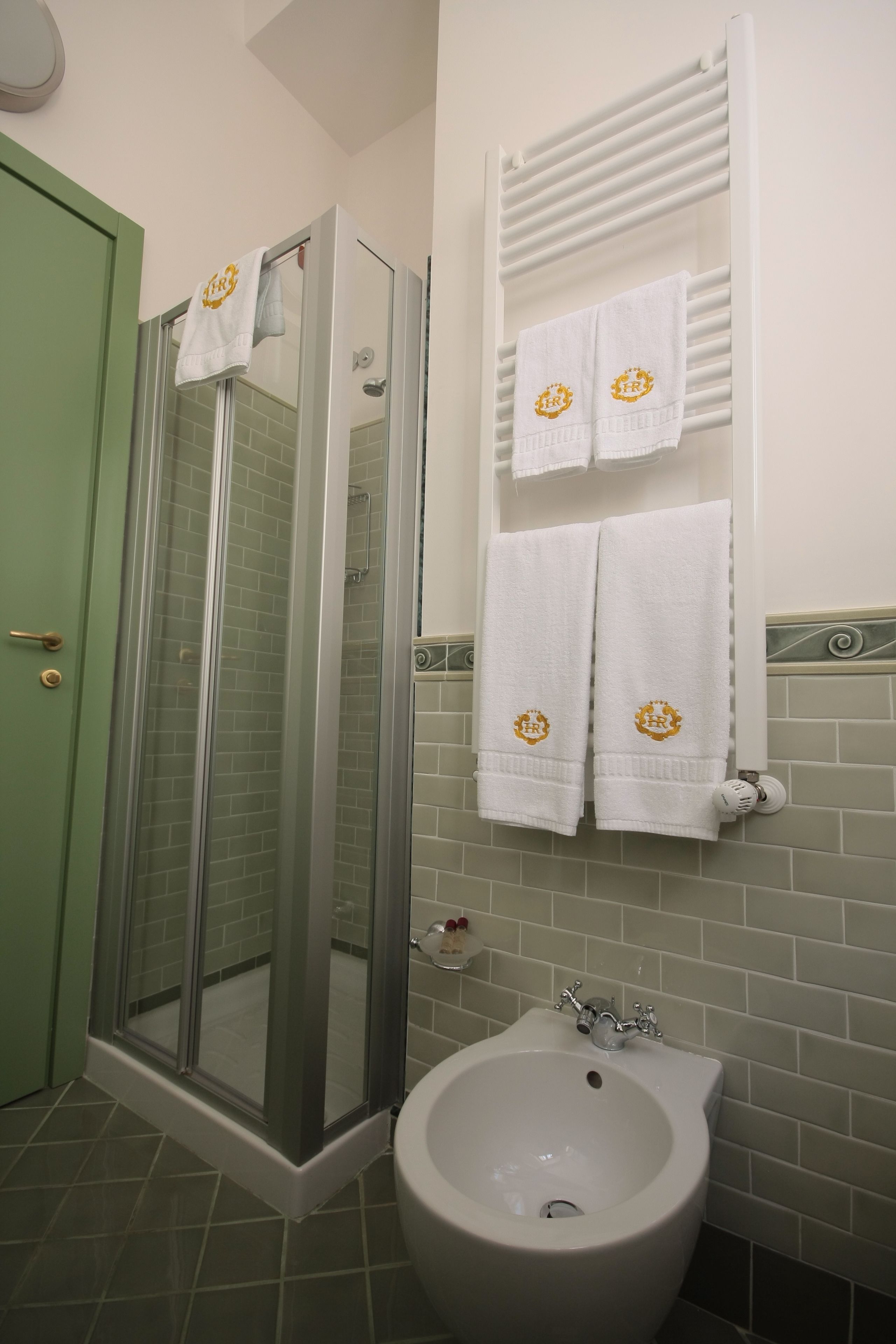 Casa de banho com cabine de duche em vidro, bidé e duas toalhas com um logótipo na parede.