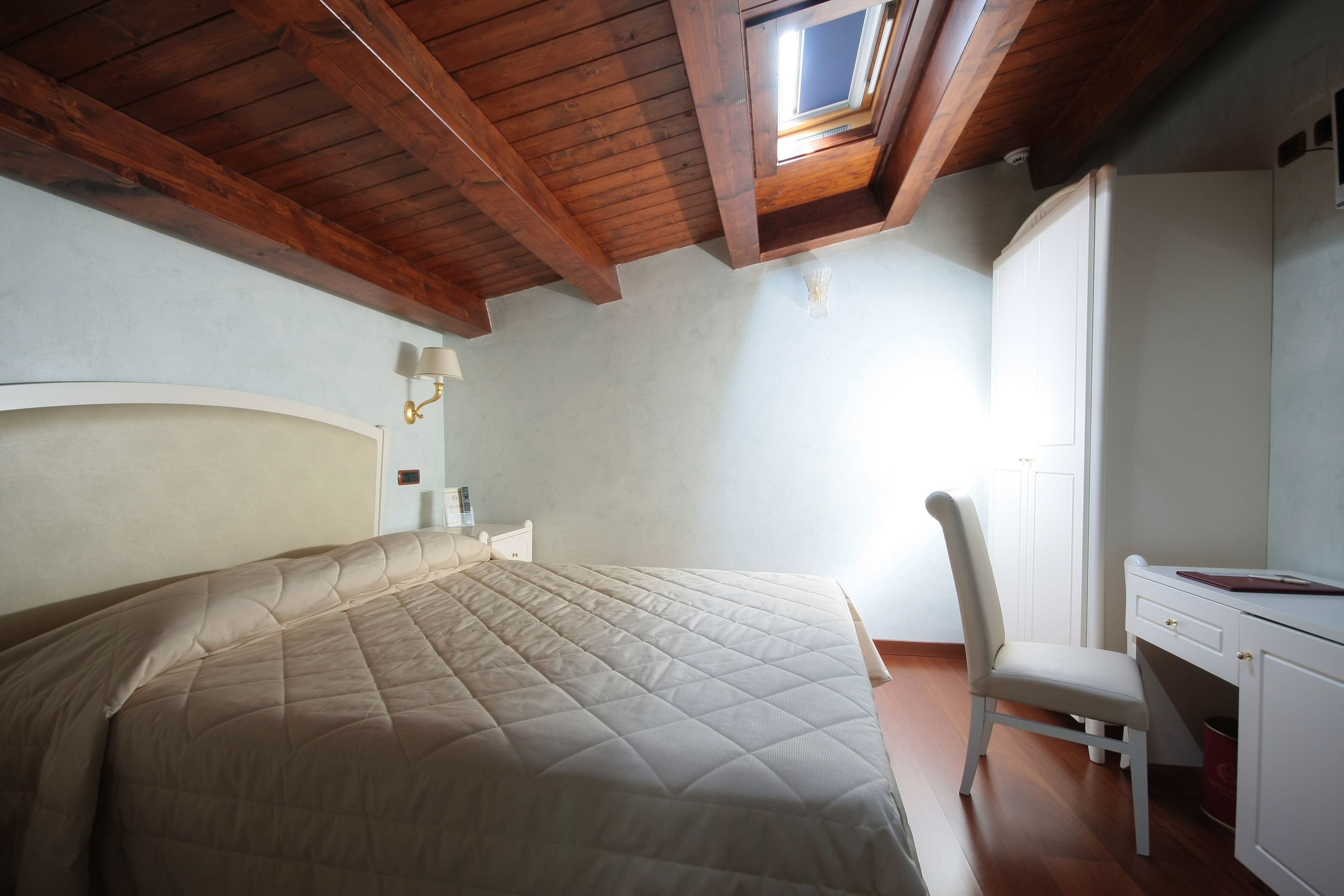 A bedroom with a large bed, a desk, and a chair. There is a skylight above the bed.