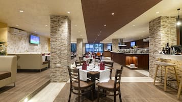 A modern dining area with stone pillars, a bar, and a kitchen in the background.