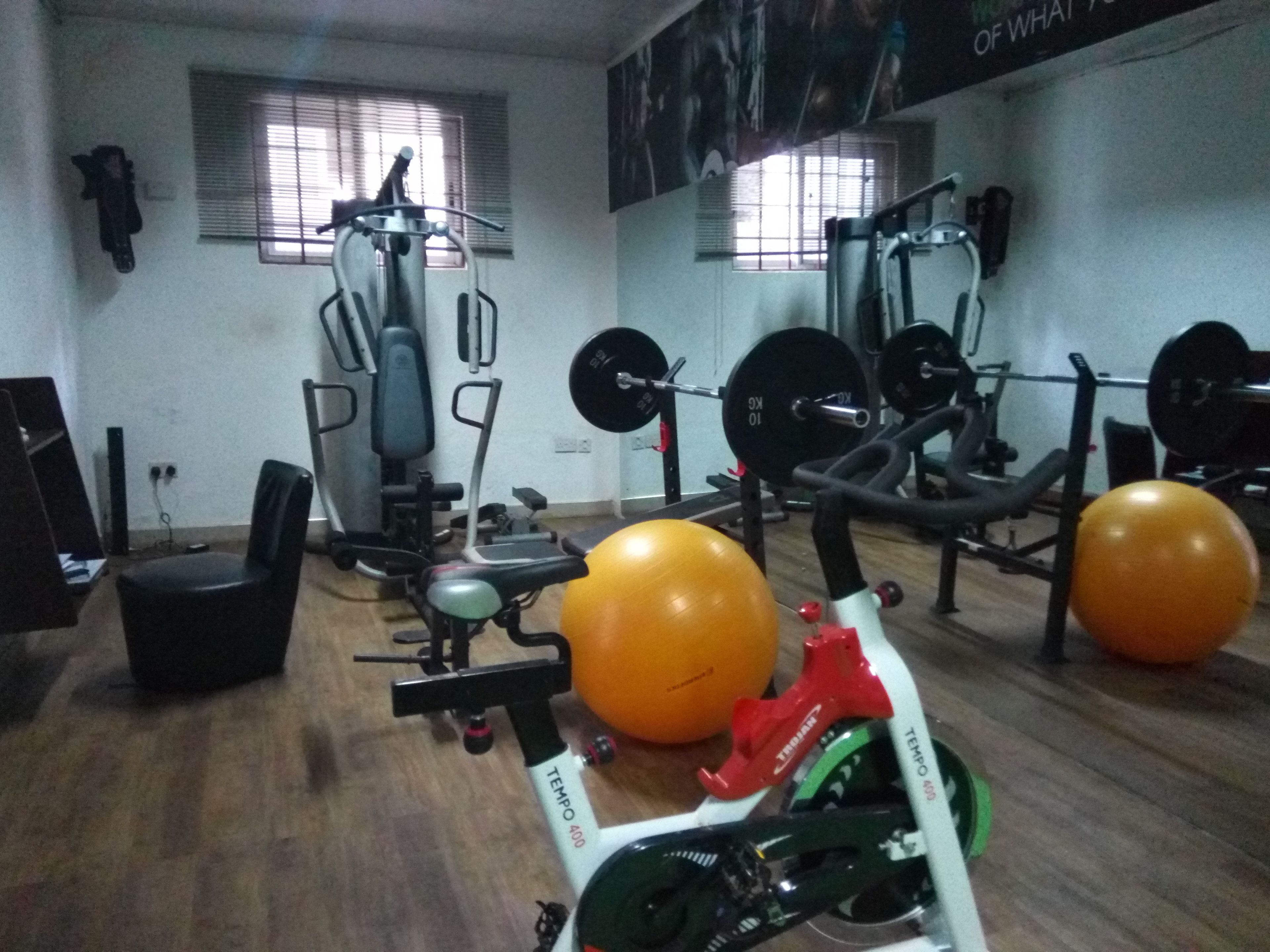 Ein Fitnessraum mit Trainingsgeräten, zwei große orangefarbene Gymnastikbälle und ein rotes und grünes Fahrrad.