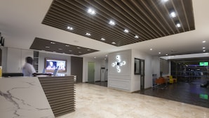 A modern lobby with a reception desk, a large screen displaying a news broadcast, and a seating area with colorful chairs.