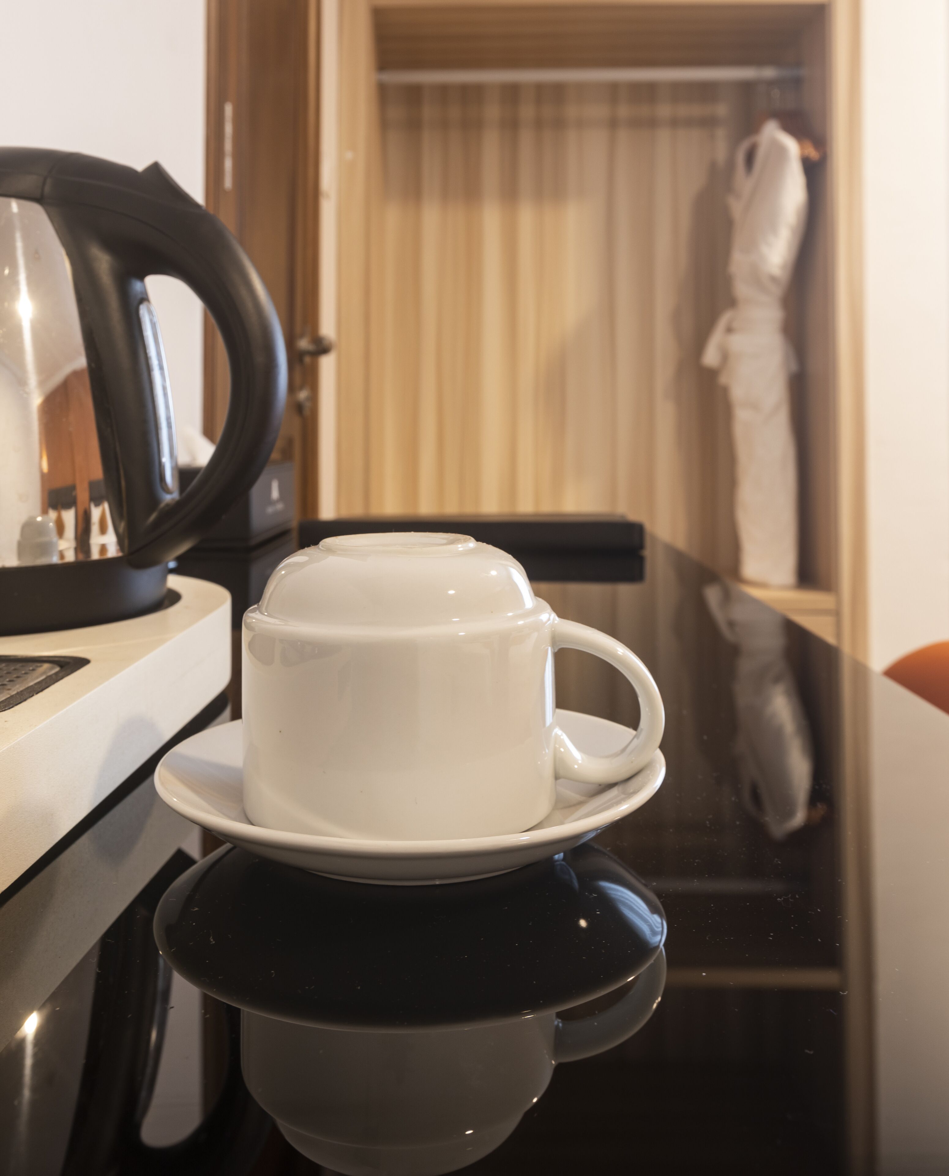 A white cup on a black saucer on a reflective surface, with a wooden door and a white towel in the background.