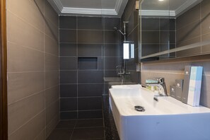 A modern bathroom with dark tiles, a white sink, and a shower. - Airport View Hotel (Accra)
