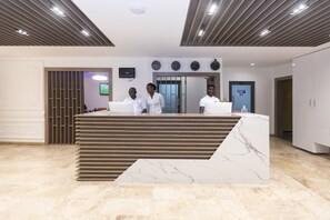 A reception area with a marble counter, a television mounted on the wall, and a door with a blue sign. - Airport View Hotel (Accra)