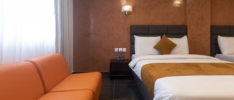 Una habitación de hotel con una cama grande, un sofá naranja, una mesita de noche con lámpara y un equipo de aire acondicionado.