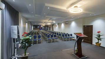Une salle de conférence avec des rangées de chaises, un pupitre et des luminaires au plafond.