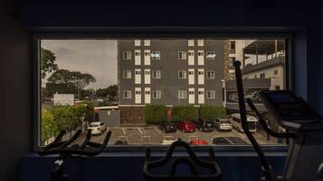 A view from a window with exercise equipment, overlooking a parking lot and a multi-story building with a "Welcome" sign.