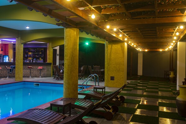 Zona de piscina con sillas de descanso, un bar y suelo a cuadros.