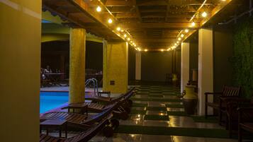 A poolside area with lounge chairs, a checkered floor, and a row of lights on the ceiling.