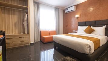 A modern hotel room with a large bed, a wooden wardrobe, an orange sofa, and a statue.
