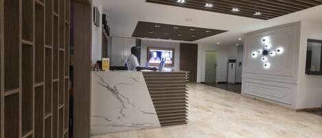 A modern reception area with a marble counter, a television screen, and a ceiling with recessed lighting.