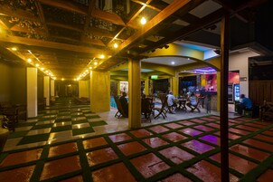 A spacious indoor area with a checkered floor, wooden columns, and a bar area with people.